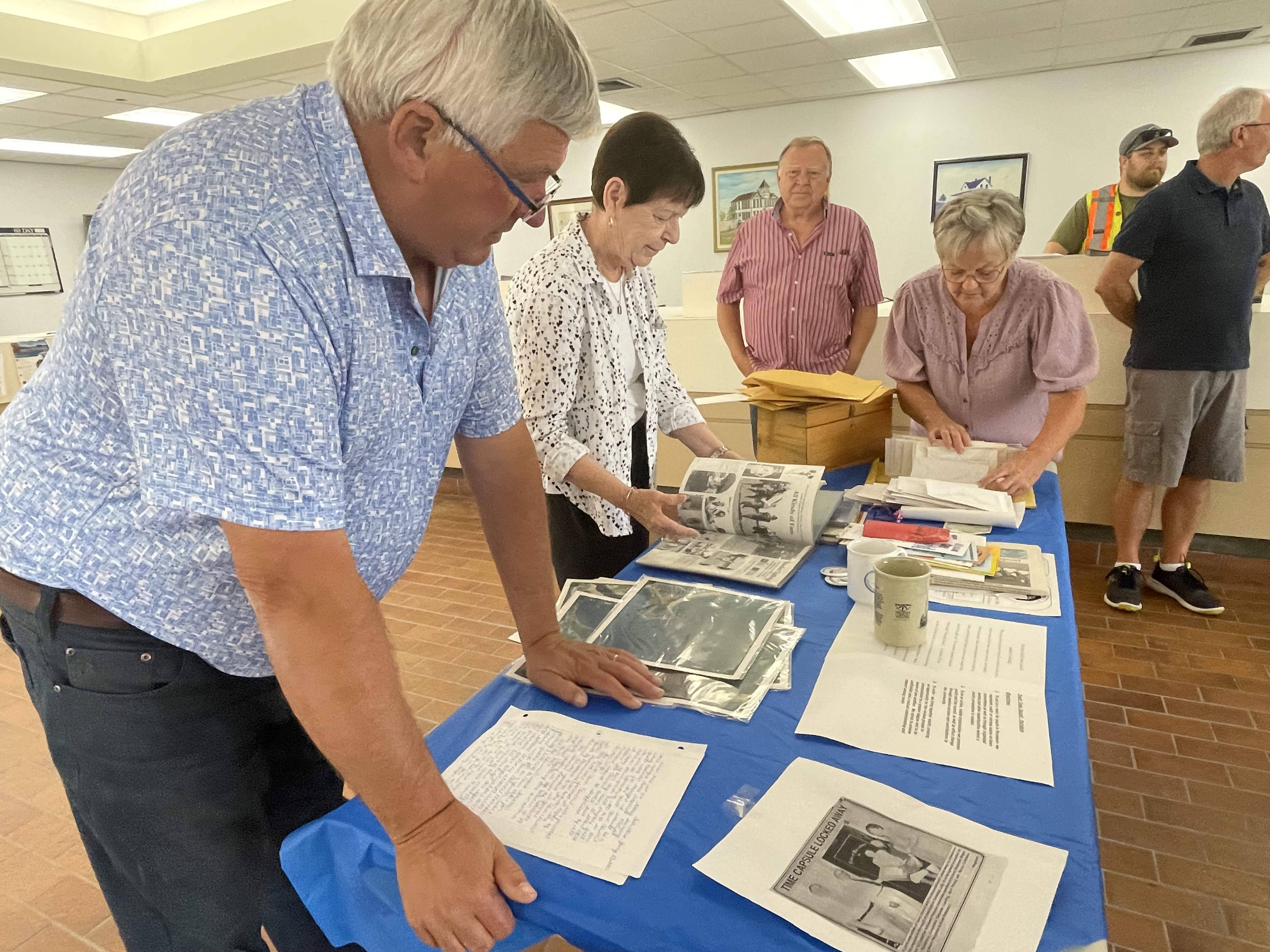 A man and two women look over a bunch of photos and papers on a table.